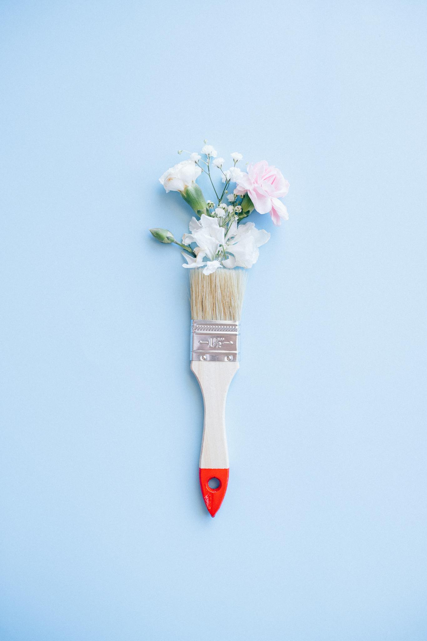 A minimalist image of a paintbrush adorned with delicate flowers against a blue background.